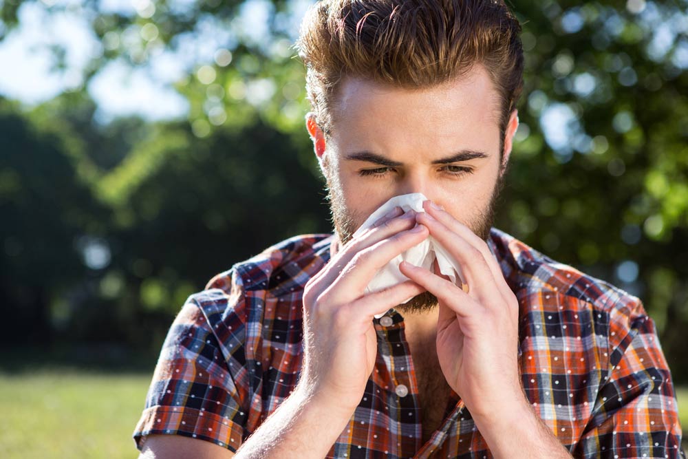 Man blowing his nose, fighting off Spring Allergies